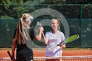 Two female tennis players shaking hands with smiles on a sunny day, exuding sportsmanship and friendship after a