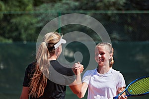 Two female tennis players shaking hands with smiles on a sunny day, exuding sportsmanship and friendship after a