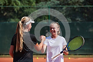 Two female tennis players shaking hands with smiles on a sunny day, exuding sportsmanship and friendship after a