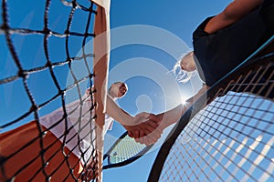 Two female tennis players shaking hands with smiles on a sunny day, exuding sportsmanship and friendship after a