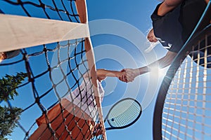 Two female tennis players shaking hands with smiles on a sunny day, exuding sportsmanship and friendship after a