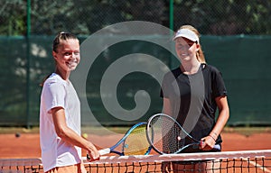 Two female tennis players shaking hands with smiles on a sunny day, exuding sportsmanship and friendship after a