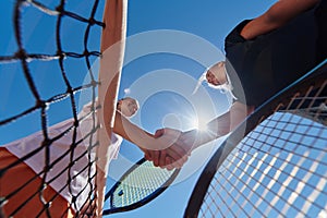 Two female tennis players shaking hands with smiles on a sunny day, exuding sportsmanship and friendship after a
