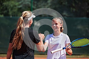 Two female tennis players shaking hands with smiles on a sunny day, exuding sportsmanship and friendship after a