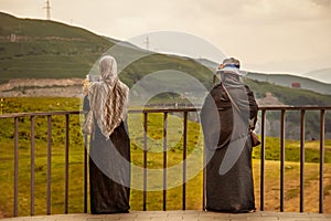 Two female tourists in Abaya and HijÃÂb checks phone standing atGeorgia Friendship Monument on Military Highway - one takig photo