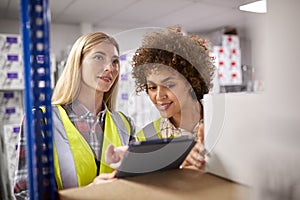 Two Female Workers In Logistics Distribution Warehouse Using Digital Tablet