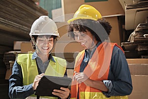 Two female workers in safety uniforms check a pile of stock in a paper factory