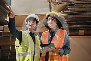 Two female workers in safety uniforms check a pile of stock in a paper factory