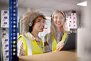 Two Female Workers Wearing Headsets In Logistics Distribution Warehouse Using Digital Tablet