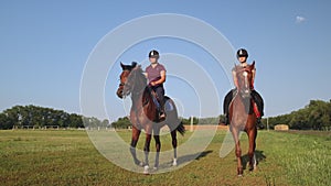 Two females are riding horses along country racetrack