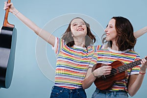 Two feminist joyful twin girls playing guitar and ukulele