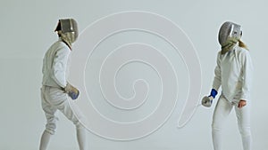 Two fencers have fencing training on white background indoors