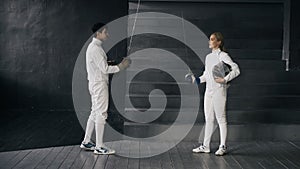 Two fencers man and woman have greeting each other and start fencing match indoors