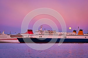 Two ferries moored by pier during colorful sunset and moonrise in port