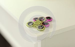 Two fidget spinners pink and green stress relieving toy on white shelf with flowers on background closeup