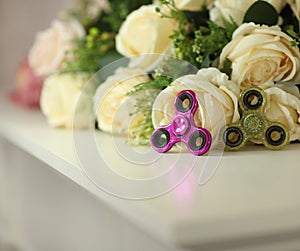 Two fidget spinners pink and green toys on white shelf with flowers on background closeup