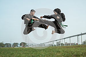 Two fighters wearing black pencak silat uniforms with flying kicks photo