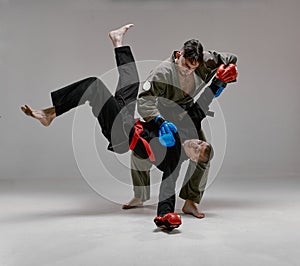 Two fighting guys in kimono and boxing gloves during battle, knockout, martial arts, mixed fight concept