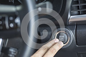 Two Finger pressing the Engine start stop button of a car