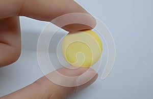 Two fingers of left hand holds a vitamin C tablet, isolated on the white background.