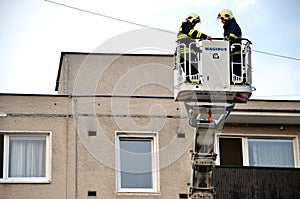 Two firefighters uprise into telescopic boom basket of fire truck, block of flats in background