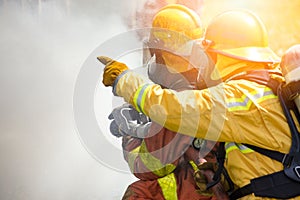 two firefighters water spray high pressure nozzle to fire surround by smoke with flare and copy space