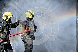 Two fireman or firefighters stand and help each other to spray of water with curtain shape and rainbow reflex occur on water