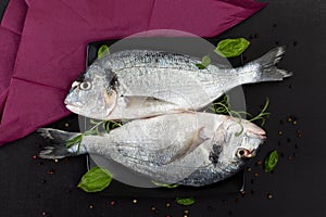 Two fish with fresh herbs on black plate.