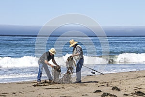 Two Fishermen at a daytime beach untangle lines from seaweed