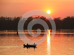 Two fishermen, a man and a woman, swim in a motor boat on the river against the background of an orange sunset. Romantic