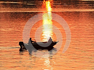 Two fishermen, a man and a woman, swim in a motor boat on the river against the background of an orange sunset. Romantic