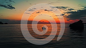 Two fishermen in a small wooden boat are fishing in a sunset in Golden bay, Malta