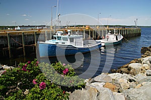 Two fishing boats moored at pier with rocks in foreground.