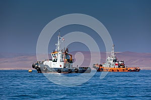 Two fishing boats stand in the sea against the backdrop of desert mountains in the ocean. Fishing boats at sea.