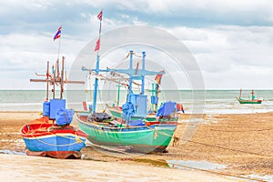 Two fishing boats stand on a shallows, low tide of the ocean with Thai flags