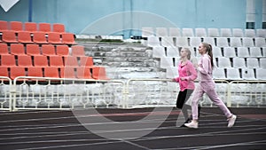 Two fit caucasian identical twin sisters in sportswear running on stadium track