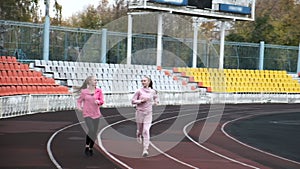 Two fit caucasian identical twin sisters in sportswear running on stadium track