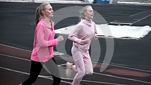 Two fit caucasian identical twin sisters in sportswear running on stadium track