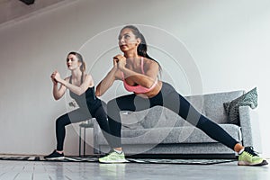 Two fit girls doing home workout performing lateral lunges at home