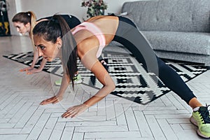 Two fit girls doing home workout performing lateral lunges at home.