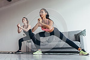 Two fit girls doing home workout performing lateral lunges at home photo
