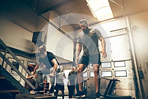 Two fit men doing box jumps together at the gym