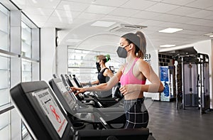 Two fit women exercising on treadmill wearing face mask in gym during pandemic