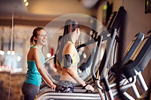 Two fit women running on treadmills in modern gym