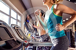 Two fit women running on treadmills in modern gym