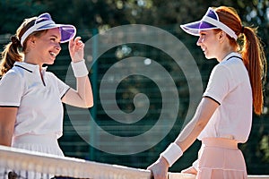 Two fit, young, tanned and healthy women playing doubles at tennis on court on vacation