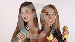 Two fitness women smiling at each other, posing with water bottle and dumbbells