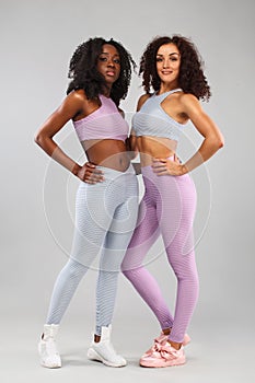 Two fitness women in sportswear isolated over gray background. Sport and fashion concept with copy space.