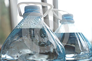 Two five-liter plastic bottles full of water, close-up of the top with lids and handles