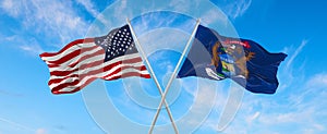 two flags of USA and state of Michigan waving in the wind on flagpoles against sky with clouds on sunny day